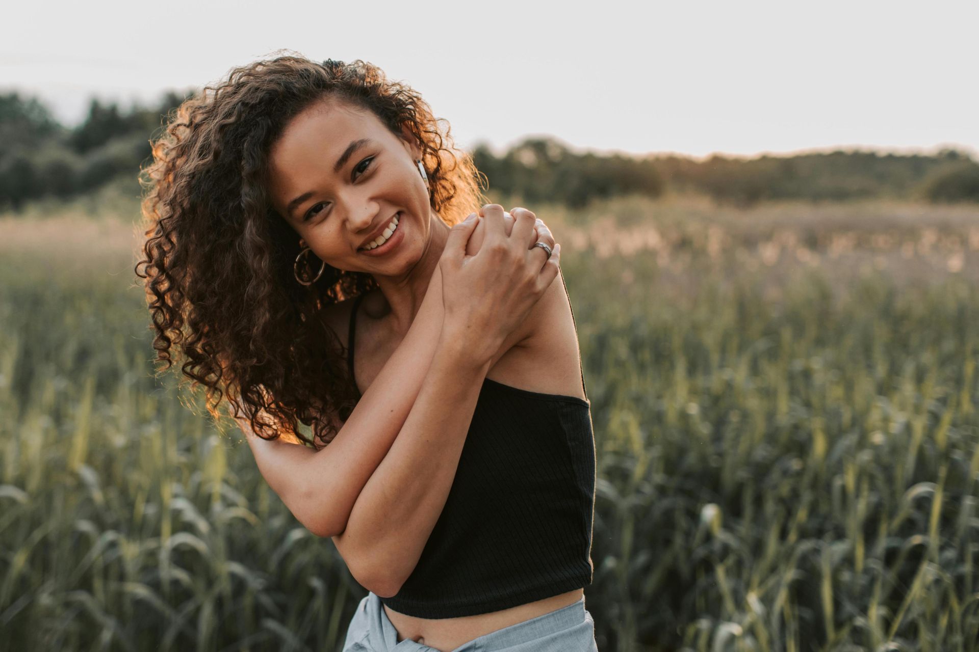 Joyful woman with curly hair smiling in a sunlit field, exuding carefree happiness.